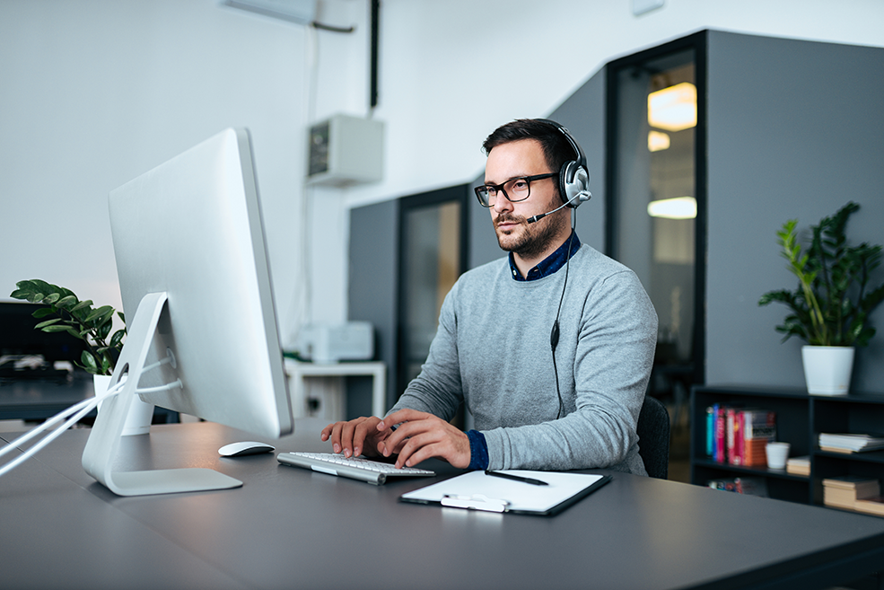 Joven especialista en TI con auriculares trabajando con analítica de infraestructura en una computadora.